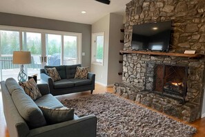 A living room with a stone fireplace, a television mounted above it, and a sofa with patterned cushions. - 550 Massive 4 Bedroom Home Sleeps 19 (Candler)