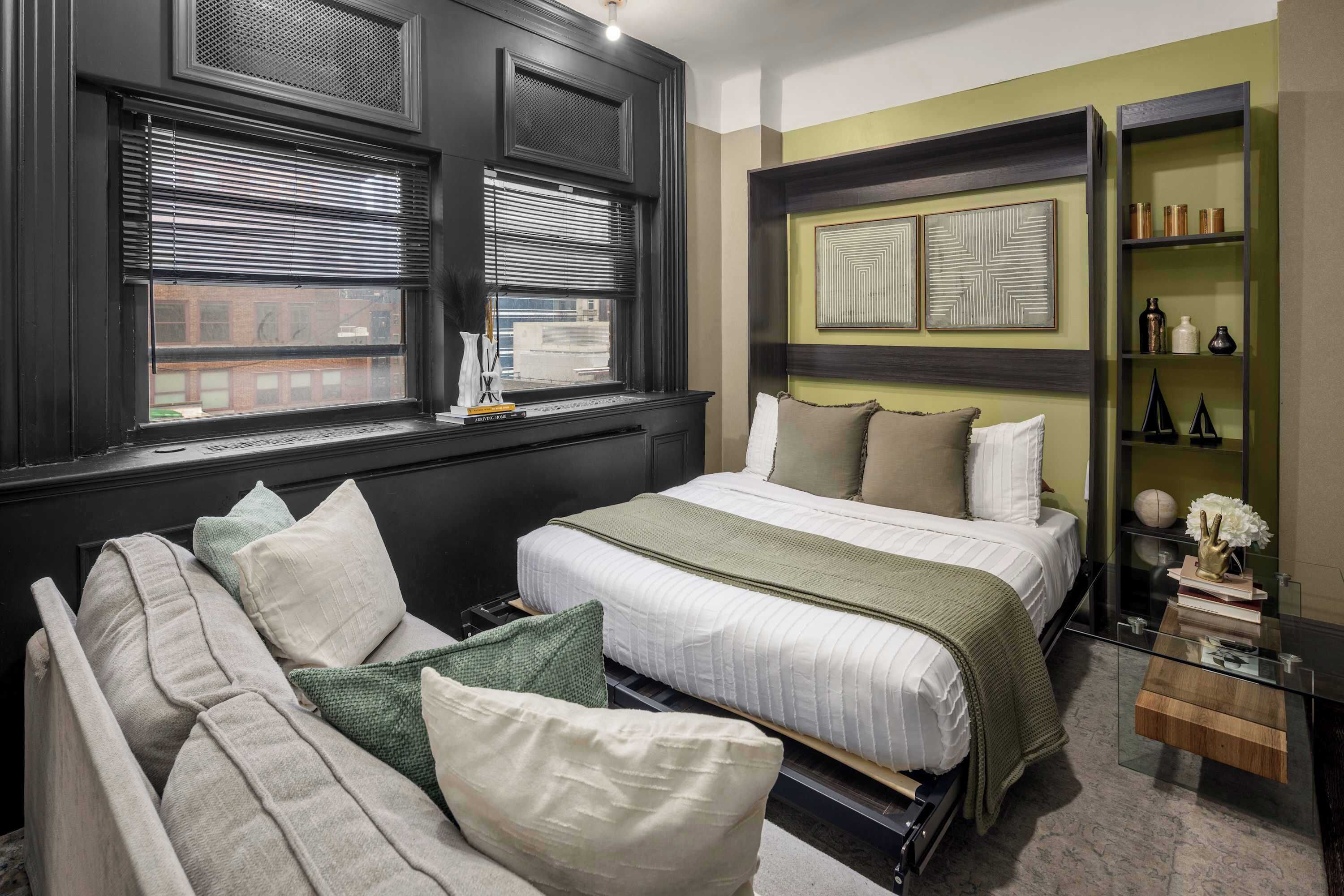 A bedroom with a bed, a sofa, a glass coffee table, and a bookshelf.