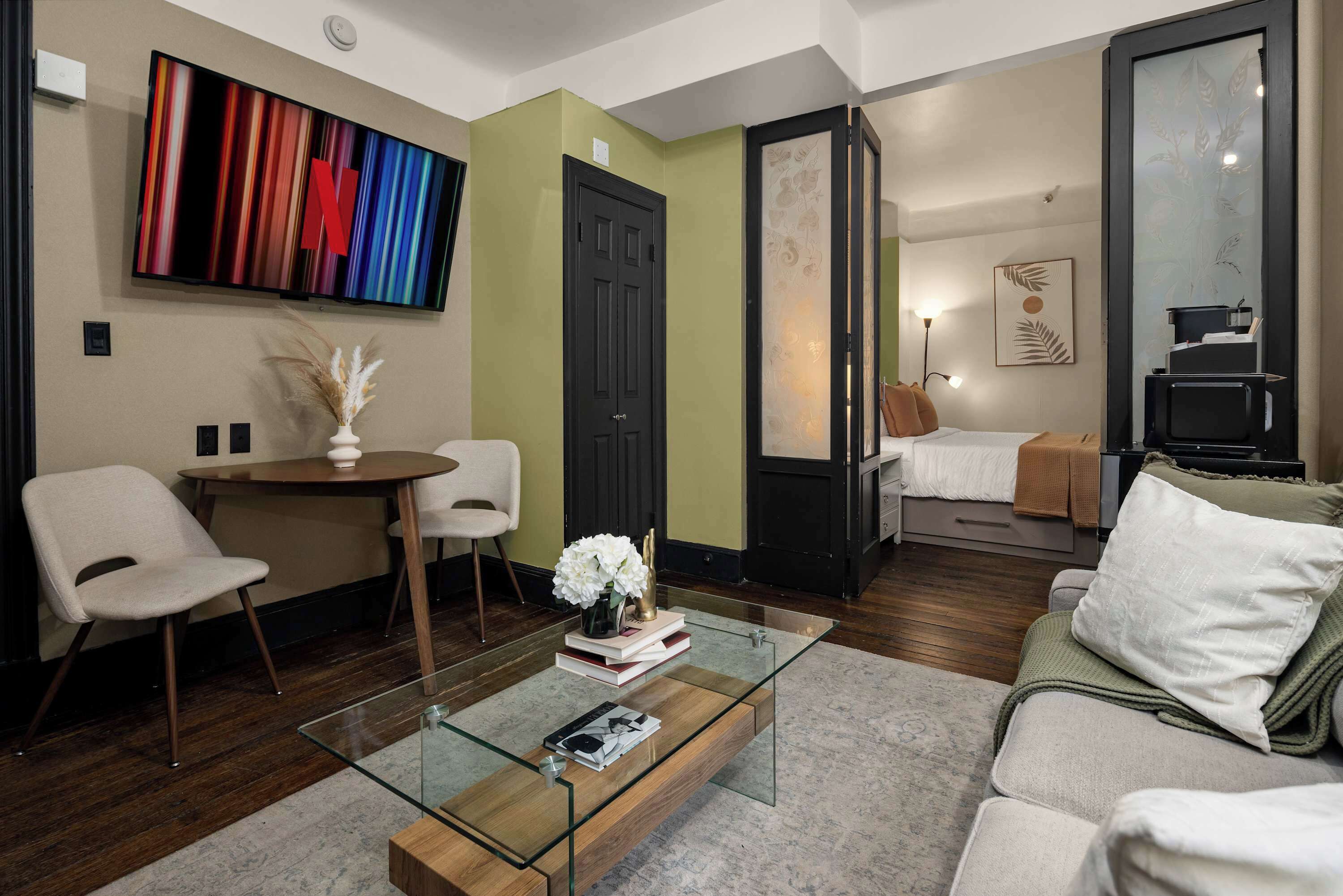 Un saló modern amb una taula de centre de vidre, un sofà, un televisor fixat a la paret i una porta que dona a una altra habitació.