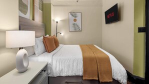 A neatly arranged hotel room with a bed, a bedside table with a lamp, a wall-mounted TV, and a framed artwork. - Centrally Located APT in NYC Walk to Time Square (New York)