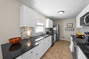 A modern kitchen with white cabinets, a black countertop, and a stainless steel refrigerator. - 564 Massive 5 Bedroom With hot tub Close to Plaza (Kansas City)