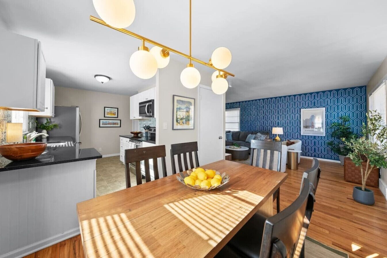 A modern kitchen with white cabinets, a black countertop, and a wooden dining table with a bowl of lemons.