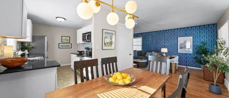A modern kitchen with white cabinets, a black countertop, and a wooden dining table with a bowl of lemons.
