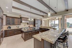 Une cuisine spacieuse dotée d’un grand îlot central, de meubles de cuisine en bois foncé et d’un lustre moderne.