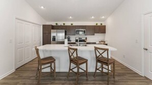 A modern kitchen with a central island, wooden chairs, and built-in appliances. - 561l Stunning Home, Pool Access, Garage Parking! (Okahumpka)