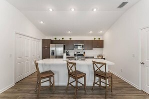 A modern kitchen with a central island, wooden chairs, and built-in appliances. - 561l Stunning Home, Pool Access, Garage Parking! (Okahumpka)