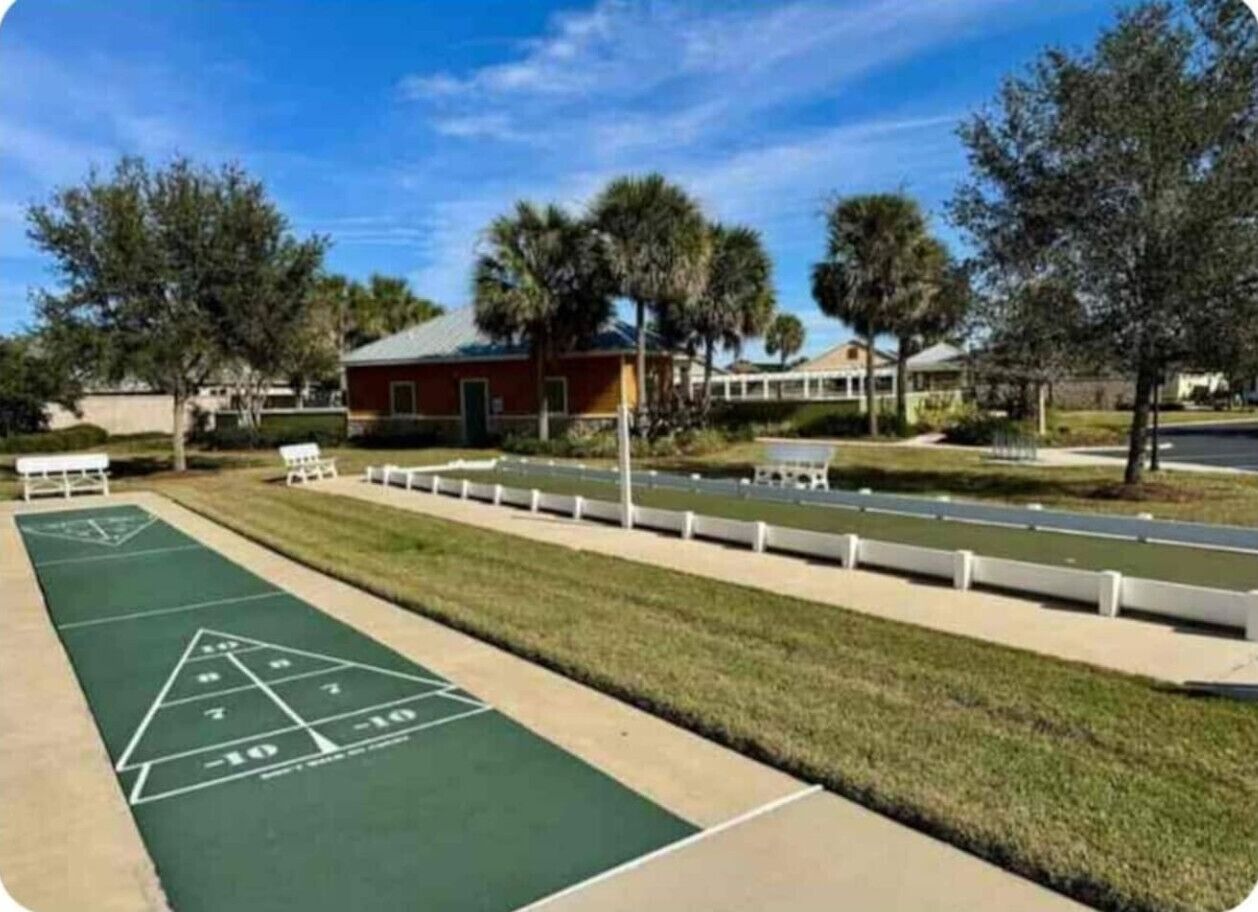 Un terrain de jeu de shuffleboard doté d’une surface verte, de lignes de démarcation blanches et d’une zone de comptage triangulaire marquée de chiffres.