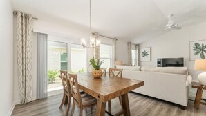 A dining area with a wooden table and chairs, a ceiling fan, and a sofa in the background. - 561l Stunning Home, Pool Access, Garage Parking! (Okahumpka)