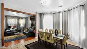 A modern living room with a black leather sofa, a glass coffee table, and a dining area with a wooden table and four chairs. - 607 Massive 5 Bedroom Close to NYC (Newark)
