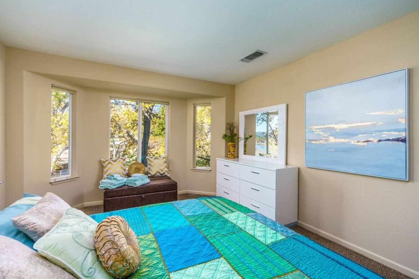 Een slaapkamer met een groot bed, een dressoir, een raam met uitzicht op bomen en een schilderij aan de muur.