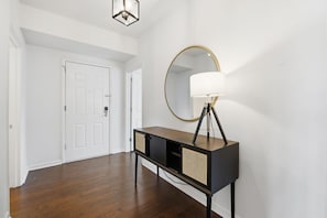Un couloir doté d’un parquet en bois foncé, d’une console noire surmontée d’un panier en osier, d’un miroir rond à cadre doré et d’un lampadaire.