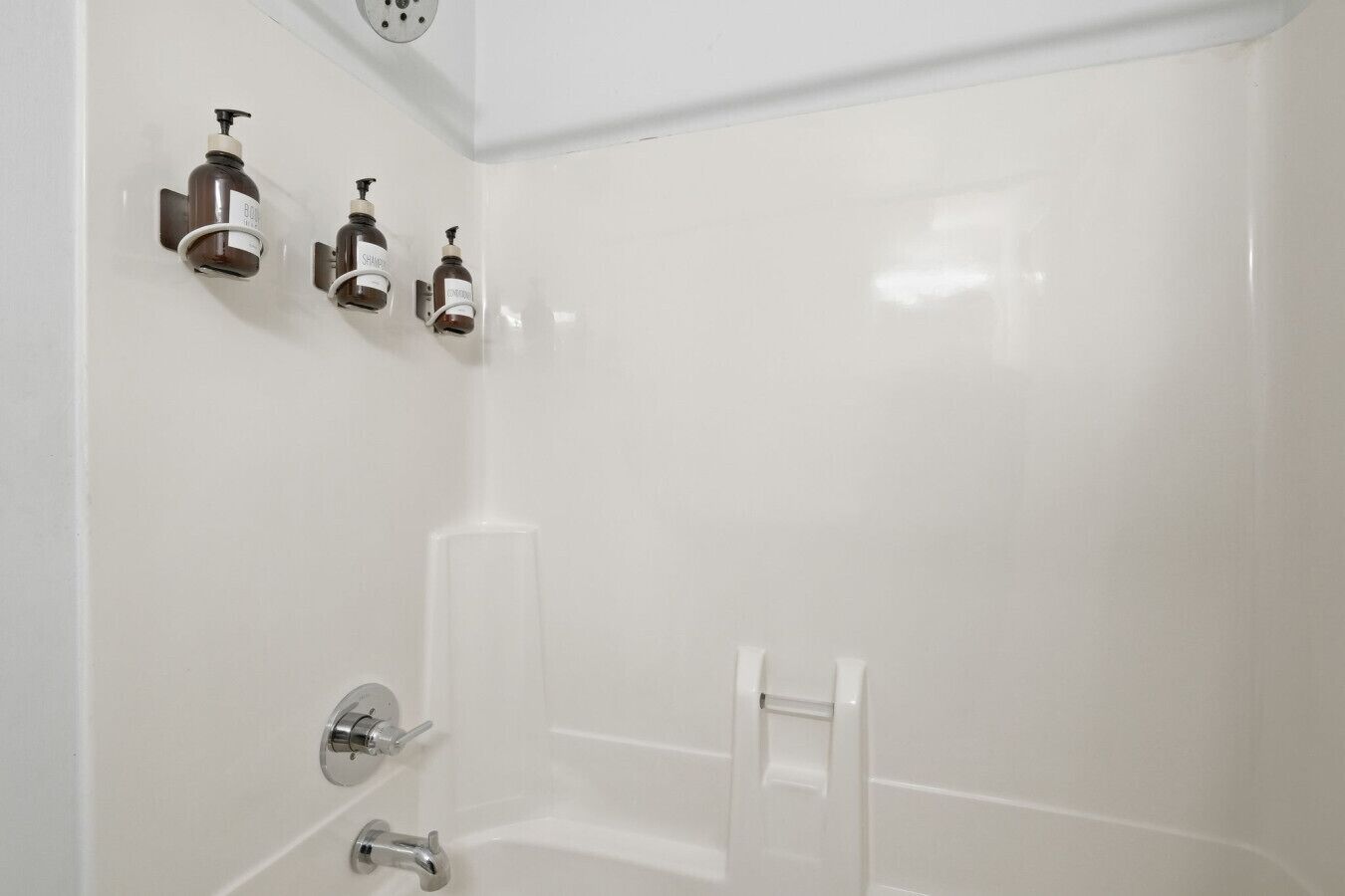 Un baño moderno con pared de azulejos blancos, zona de ducha y tres dispensadores de jabón.
