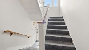 Una escalera con peldaños alfombrados y barandilla de madera, que conduce a un rellano con pared blanca y una ventana.