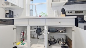 Una cocina moderna con armarios blancos, un ventanal y varios electrodomésticos, incluyendo una cafetera, una estufa y un lavavajillas.