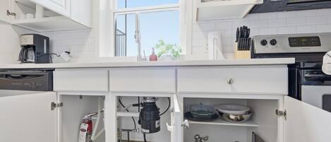 Una cocina moderna con armarios blancos, un ventanal y varios electrodomésticos, incluyendo una cafetera, una estufa y un lavavajillas.