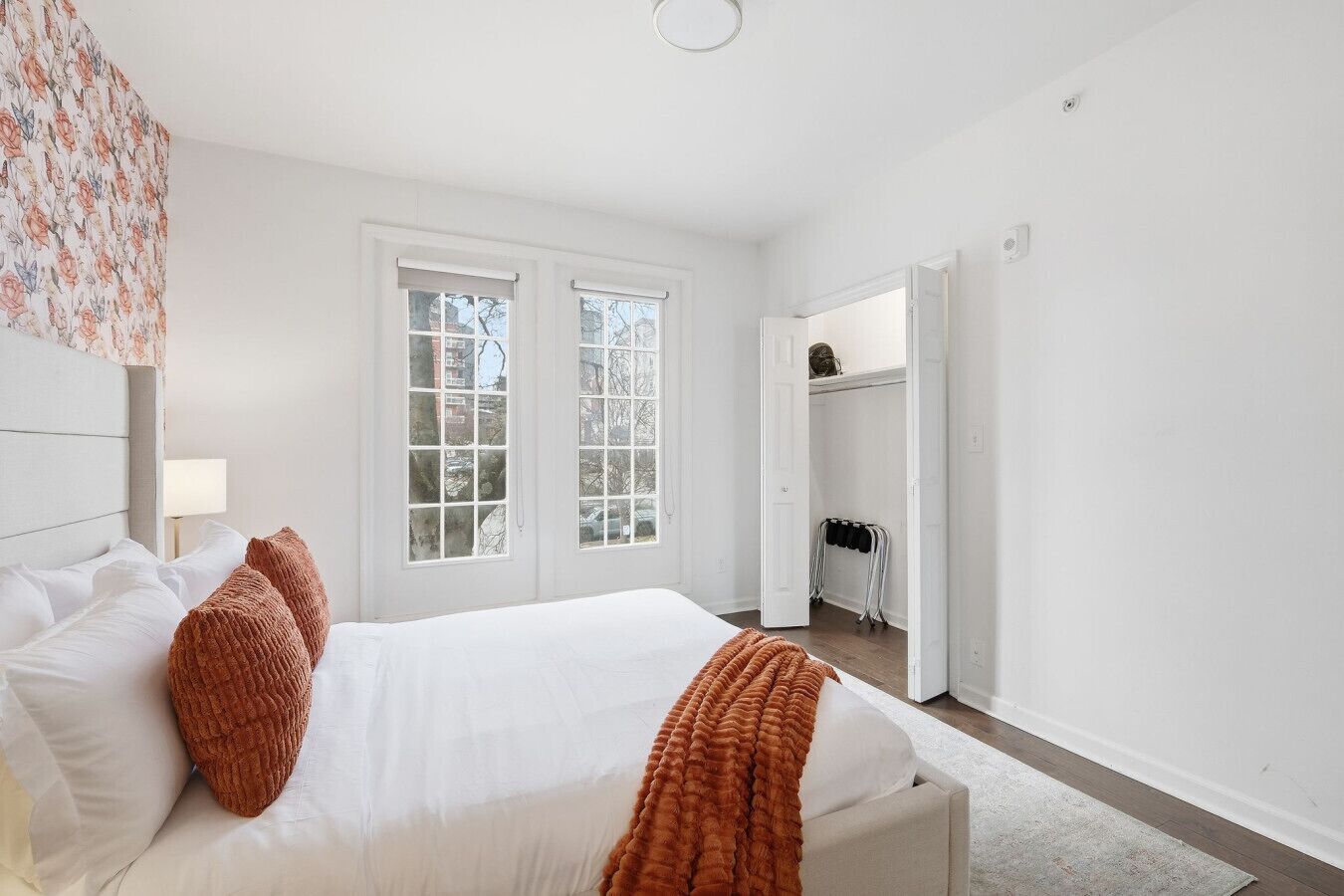 Een slaapkamer met een groot bed, twee ramen, een kledingkast en een deur naar een andere kamer.