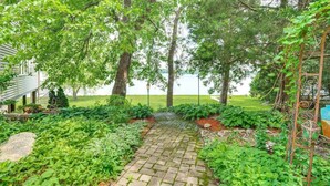 A paved garden path leading to a wooden bench, surrounded by lush greenery and trees. - 519c On the Lake Hot Tub Pool Table 10 Beds (Howard Lake)