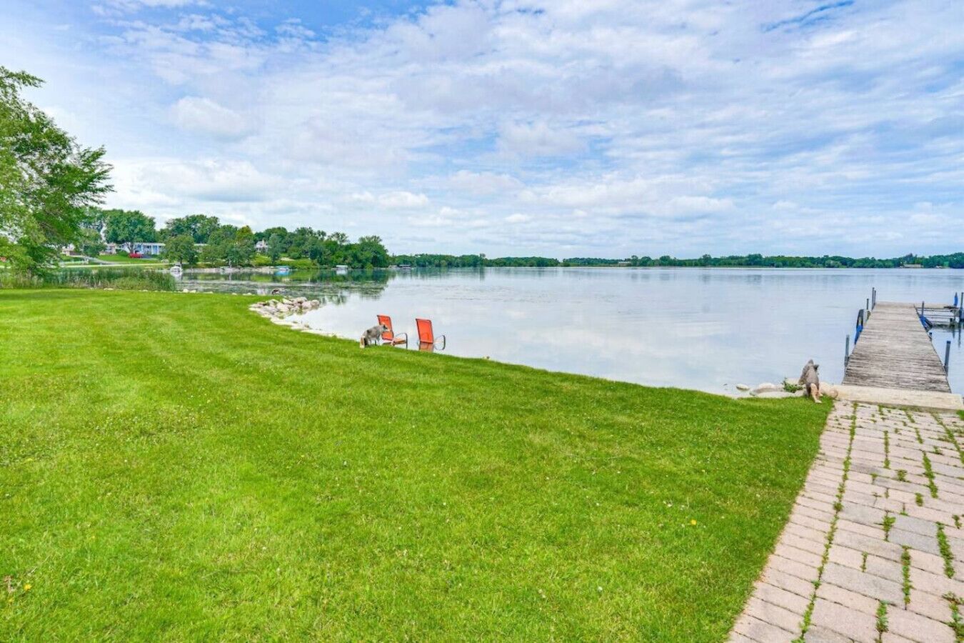 A grassy area with a dock extending into a calm lake, surrounded by trees and a clear sky.