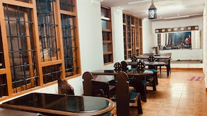A library with multiple tables and chairs, wooden bookshelves, and a tiled floor.