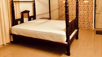 Una cama con dosel de madera con un colchón blanco en una habitación con paredes de baldosas y suelo de madera.