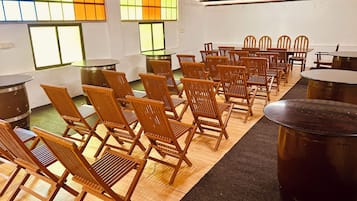 Une pièce avec des rangées de chaises et de tables en bois, de grands tonneaux en métal et des fenêtres aux vitres teintées de vert.