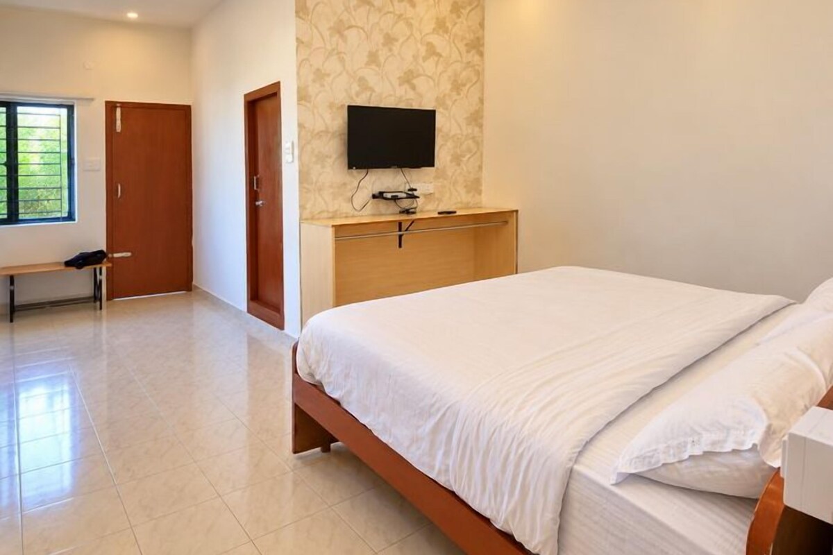 Un dormitorio con cama, televisor montado en la pared y un banco en la esquina.