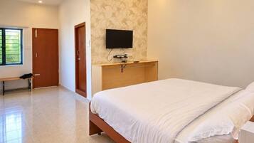 A bedroom with a bed, a television mounted on the wall, and a bench in the corner.