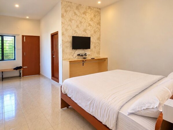 A bedroom with a bed, a television mounted on the wall, and a bench in the corner.