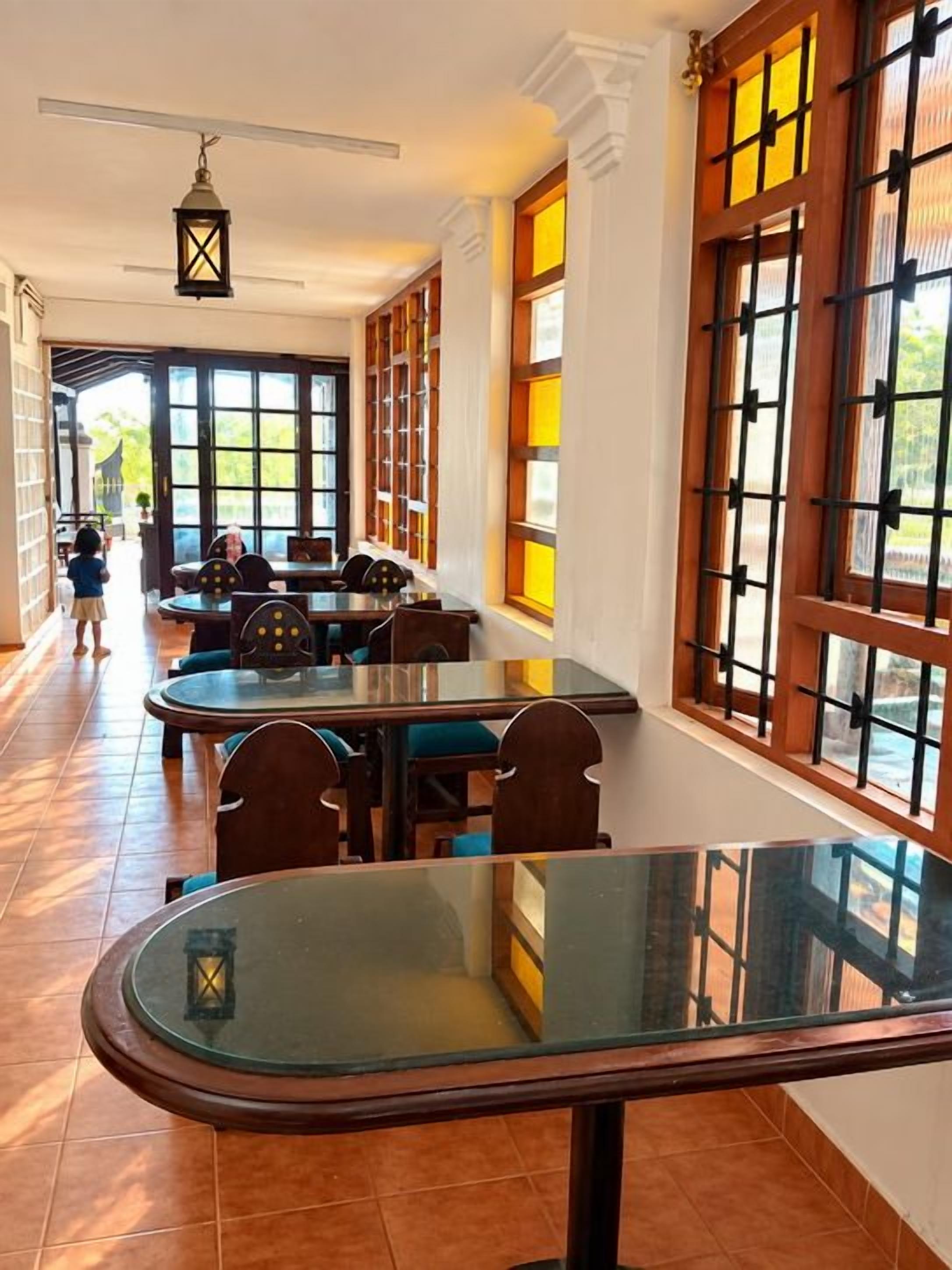 Un comedor con mesa y sillas de vidrio, ventanas amplias con marcos de madera y vista al exterior.