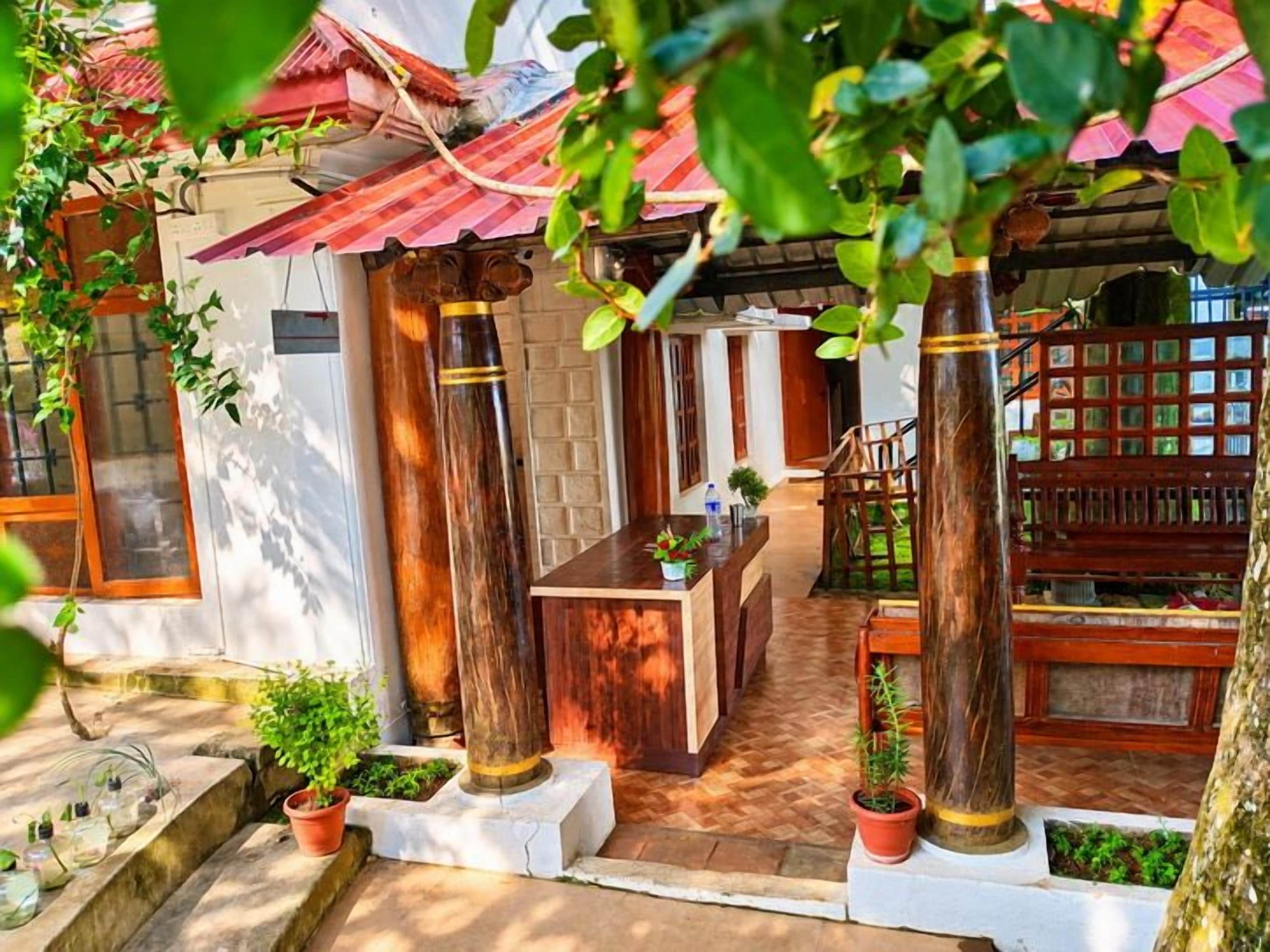 A traditional wooden structure with a tiled roof, a central seating area, and potted plants.