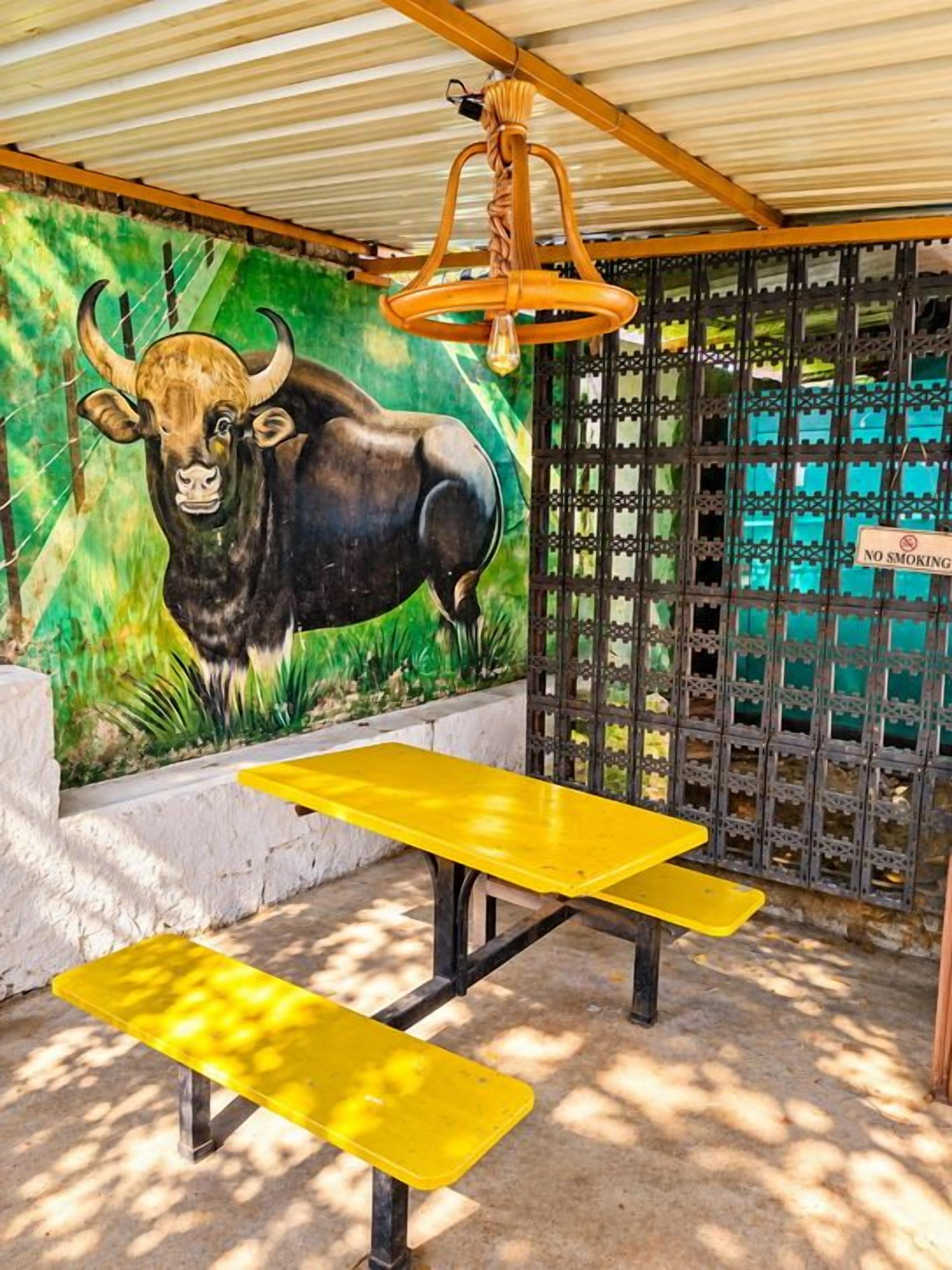 A covered outdoor area with a yellow table and benches, a mural of a bull, and a no-smoking sign.