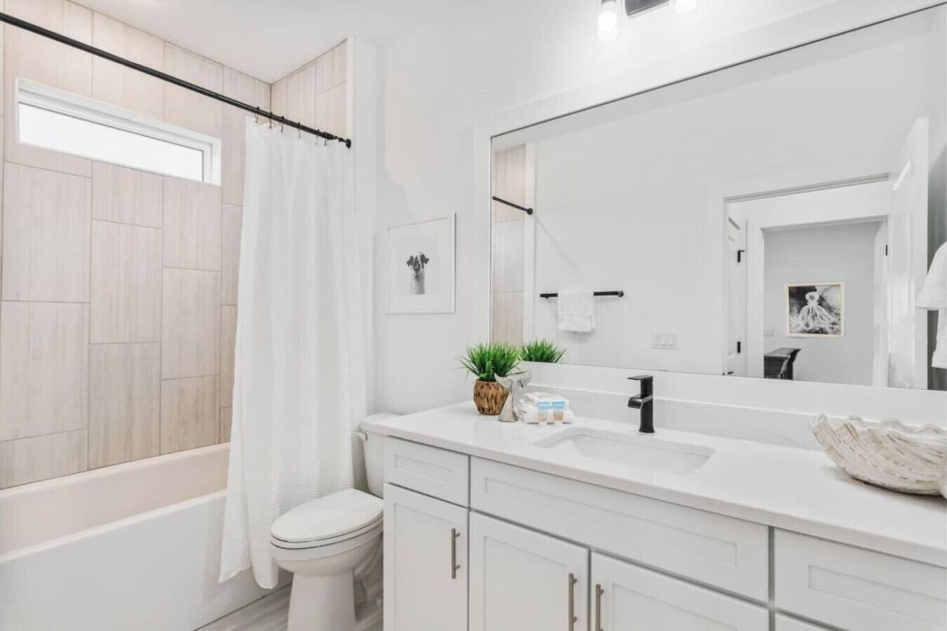 Une salle de bain moderne avec une baignoire, des toilettes, un meuble-lavabo avec un miroir et une plante en pot.