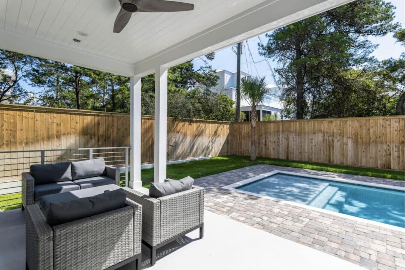 Ein überdachter Patio-Bereich mit Pool, Gartenmöbeln und Holzzaun.