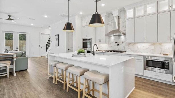 A modern kitchen with white cabinets, a large island with stools, pendant lighting, and stainless steel appliances. - 543 Private Pool Beach Golf Cart 12 Bedroom (Santa Rosa Beach)