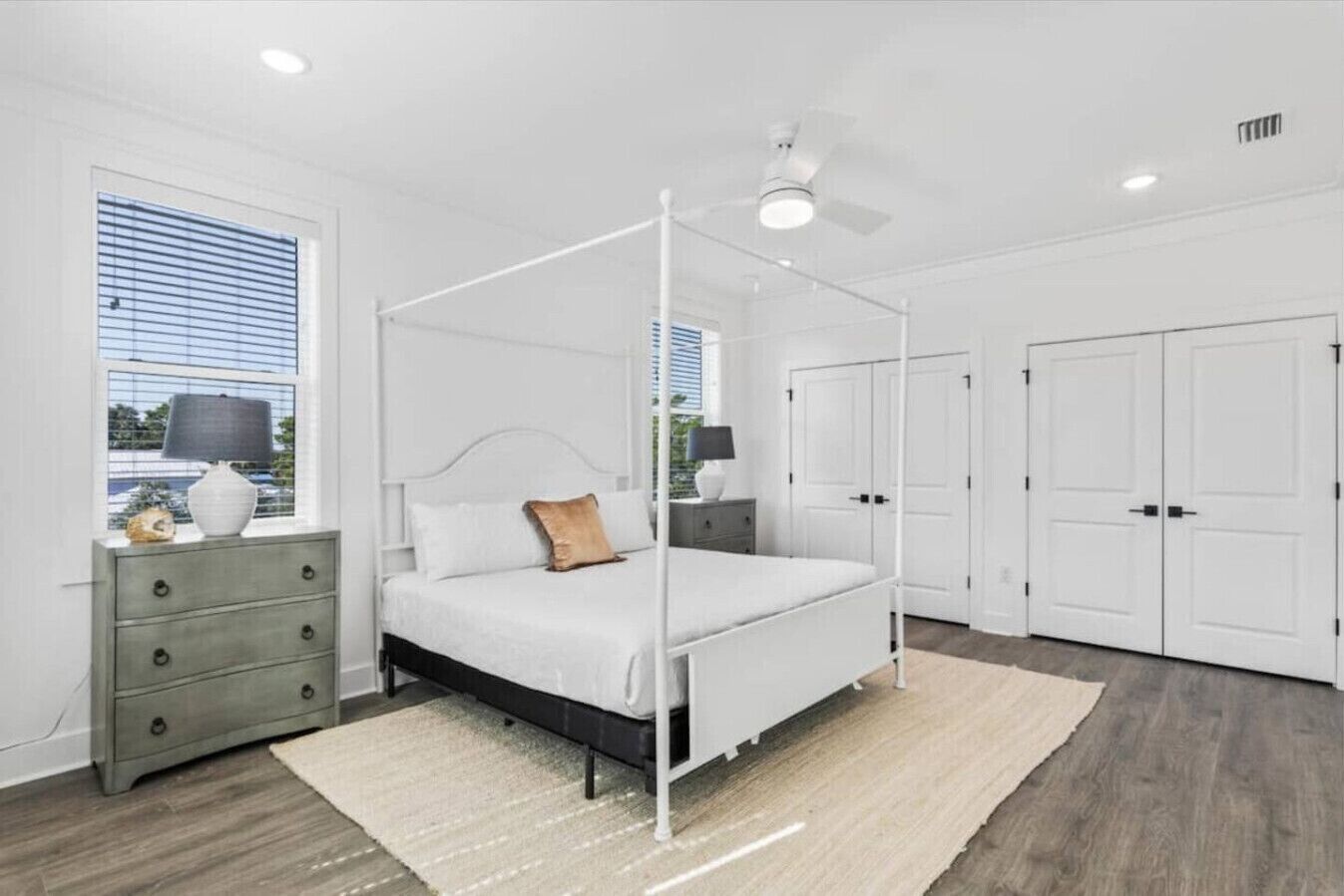 A bedroom with a four-poster bed, a nightstand, a dresser, a closet, and a window with blinds.