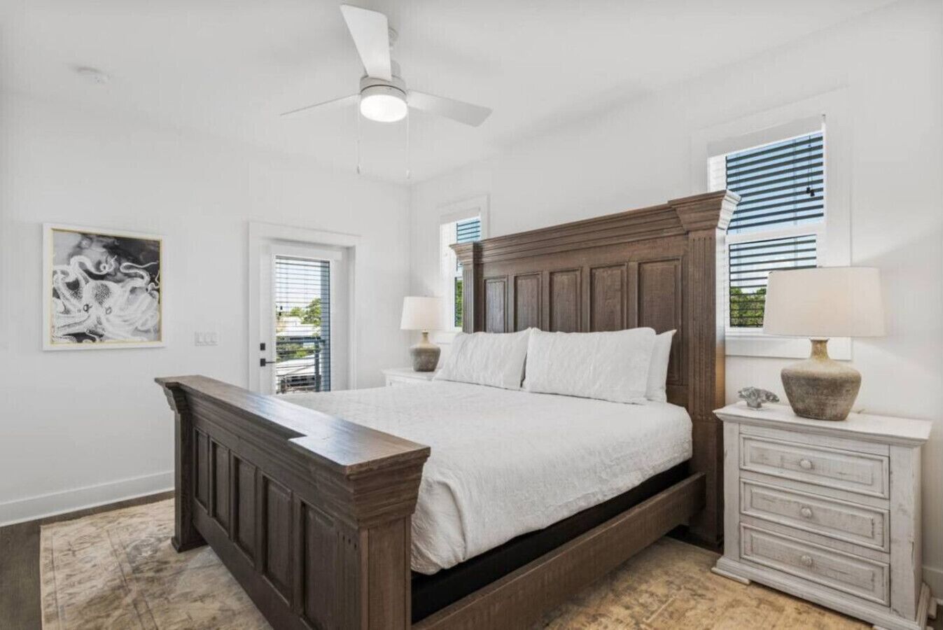A bedroom with a large bed, a wooden nightstand, a ceiling fan, and a window with blinds.