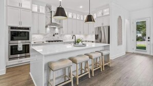 A modern kitchen with white cabinetry, stainless steel appliances, a large island with bar stools, and pendant lighting. - 543 Private Pool Beach Golf Cart 12 Bedroom (Santa Rosa Beach)