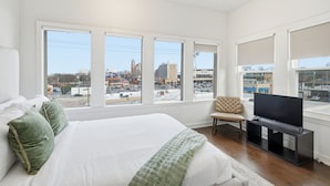 A bedroom with a large bed, a TV stand, and a chair. - Apex Executive Apartments - 30th Ave (Nashville)