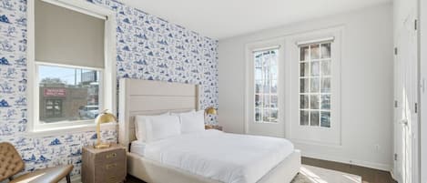 Un dormitorio con una cama grande, dos mesitas de noche, un banco y papel tapiz estampado.