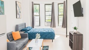 A modern room with a bed, a sofa, a TV, and a small table.