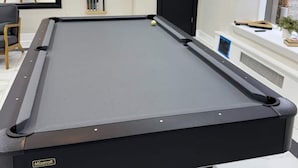 A pool table in a room with a mirror, a door, and a window.
