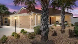 A two-story house with a garage, palm trees, and a well-maintained lawn. - 561h Large 3 Bedroom With Golf Cart Pool Access! (Wildwood)