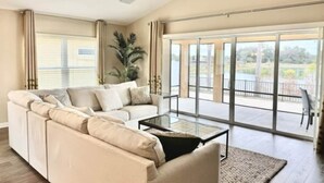 A spacious living room with a large sofa, a coffee table, and a sliding glass door leading to an outdoor area. - 561h Large 3 Bedroom With Golf Cart Pool Access! (Wildwood)