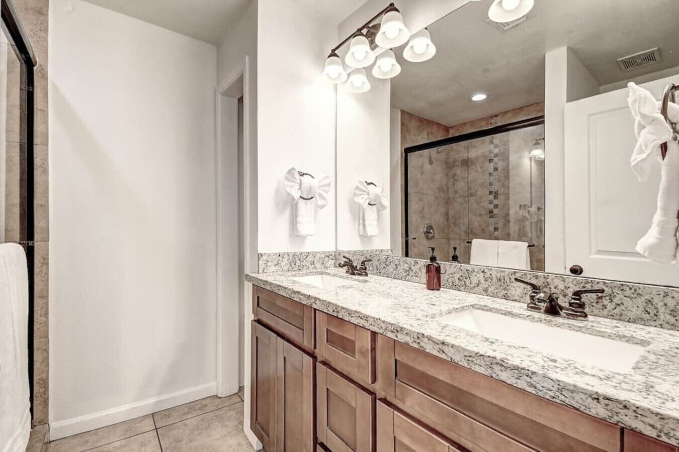A modern bathroom with a double sink, wooden cabinets, and a large mirror with lights.
