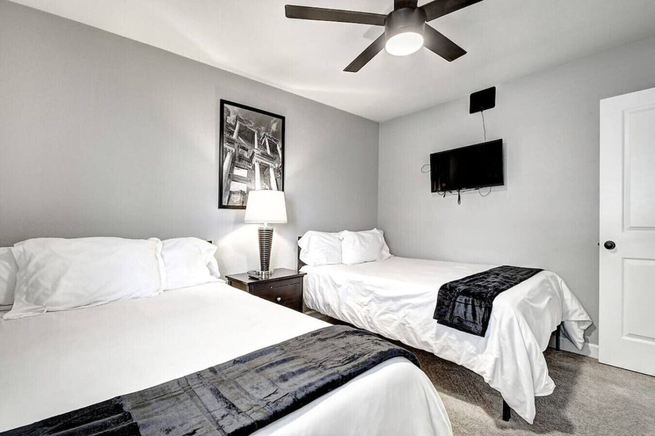 A hotel room with two beds, a ceiling fan, a mounted TV, and a framed picture on the wall.