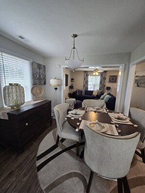 A dining area with a dark wooden table, light grey upholstered chairs, and a chandelier.