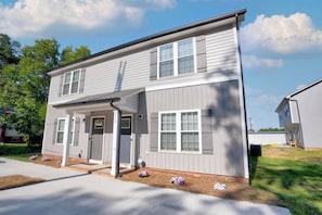 A two-story residential building with a covered porch, a front door, and a small front yard with flowers. - 611b Large 3 Bedroom Downtown Parking (Kannapolis)