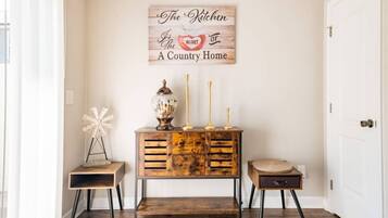 A hallway with a rustic wooden console table, a white windmill decoration, and a sign above stating "The Kitchen is the heart of a country home."
