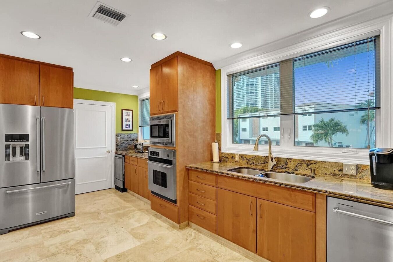 A modern kitchen with stainless steel appliances, wooden cabinets, and a large window offering a view of the city.