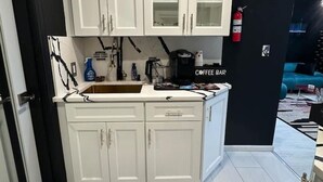 Cocina compacta con armarios blancos, una barra de café y un tapete con diseño de mármol.